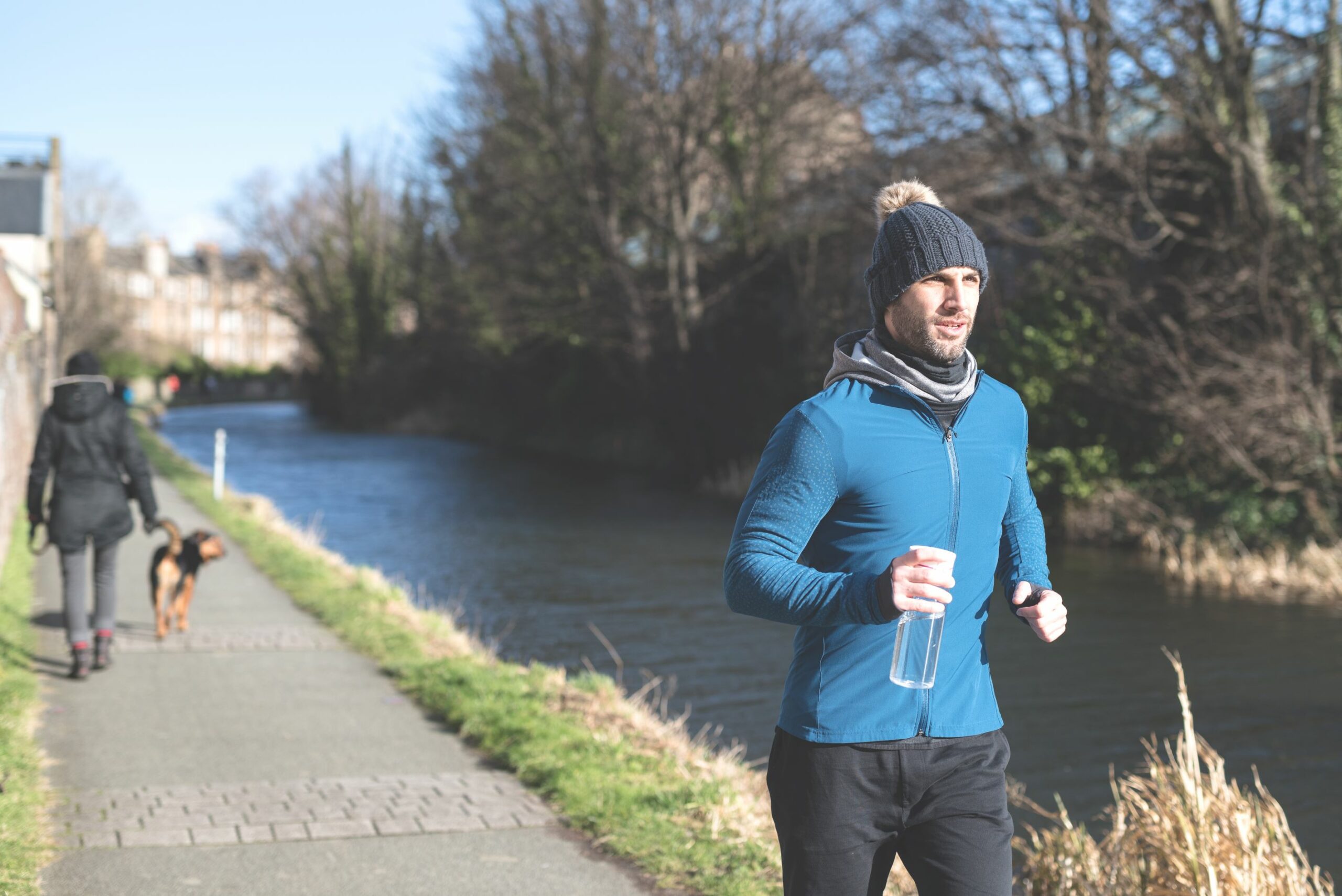 A waterway with path and a lone runner and person walking a dog