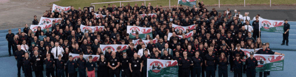 a large group of fire cadets smiles up at the camera, holding banners for the cadet games.
