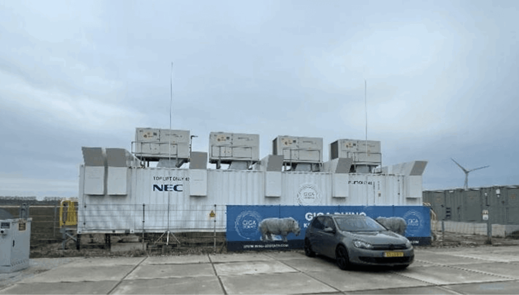 A large, white shipping container-style BESS unit situated in an open outdoor area. The internal access routes are positioned at either end of the container