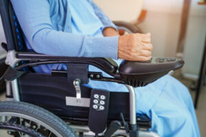 person sitting in a powered wheelchair, with their hand on the armrest joystick