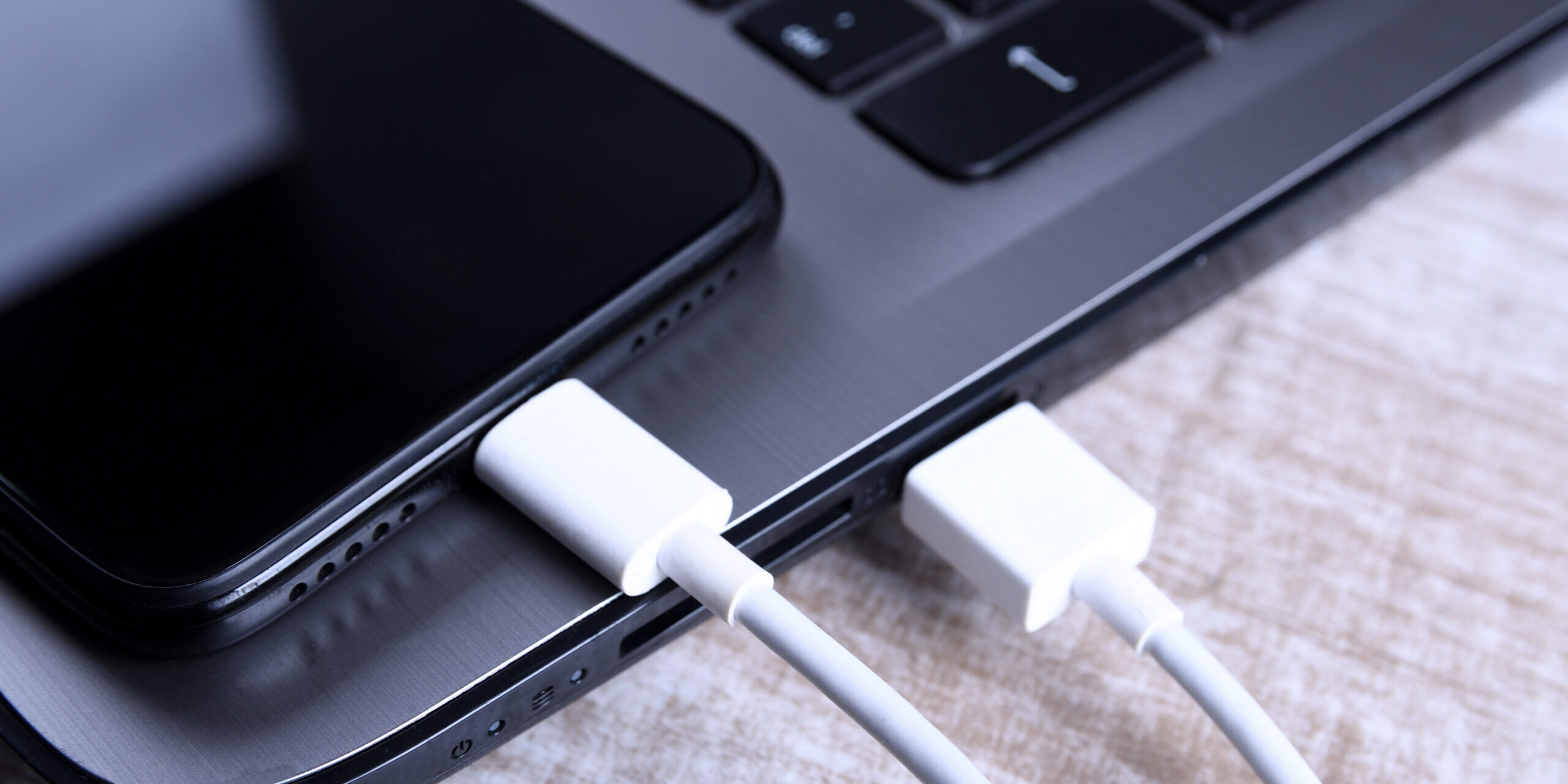 Smartphone and laptop connected to white charging cables.